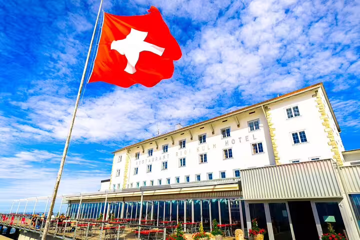 Swiss flag flutters beside Rigi Kulm Hotel under clear blue skies, highlighting Swiss hospitality.