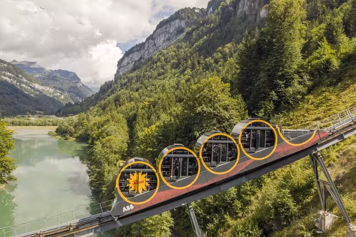 Scenic Swiss funicular railway ascending through lush green mountains with a tranquil lake view.