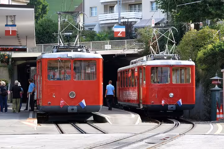Two red Swiss funiculars at a station, ready to transport visitors on the 3 Swiss Mountains in 1 Day tour.