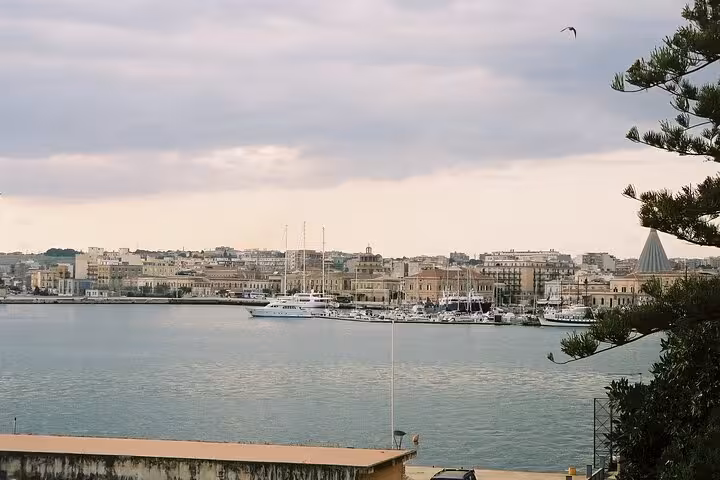 Panoramic view of Syracuse harbor with boats docked, historic buildings, and a cloudy sky creating a serene atmosphere.