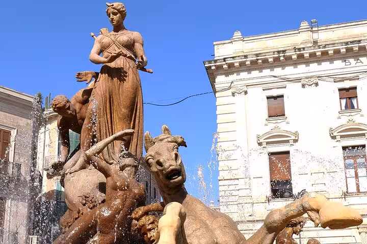 Striking fountain sculpture in Syracuse featuring dynamic figures and water jets against historic architecture.