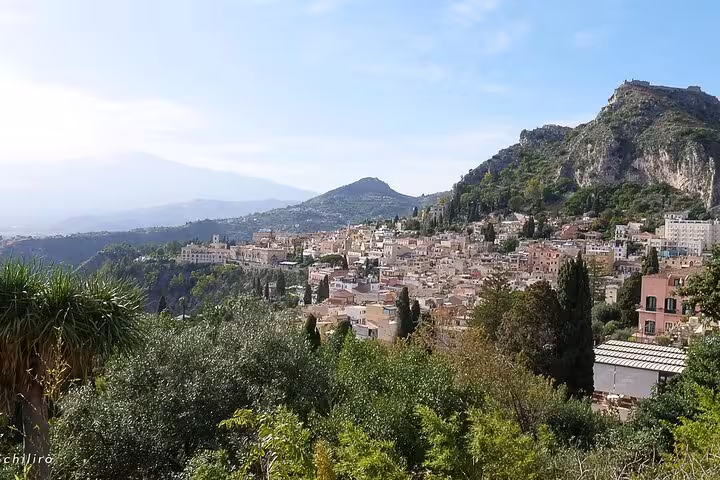 Panoramic view of Taormina nestled among lush hills with stunning Mediterranean landscape in the distance.