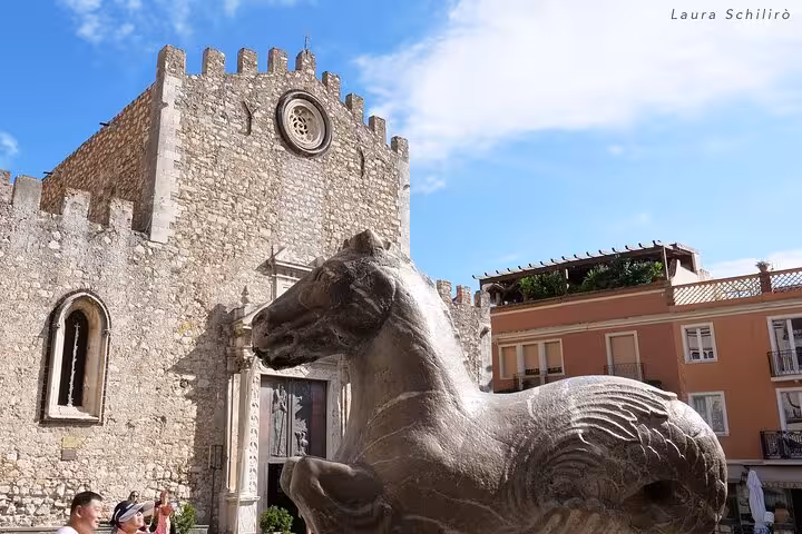 Taormina Cathedral with a prominent horse sculpture in the foreground, surrounded by sunny skies and historic charm.