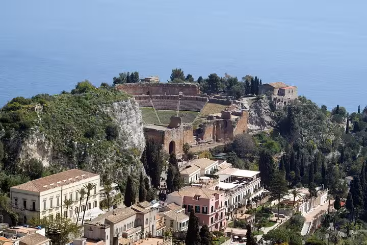 Aerial view of Taormina's Greek Theatre and charming architecture set against the vibrant blue sea, a must-visit site.