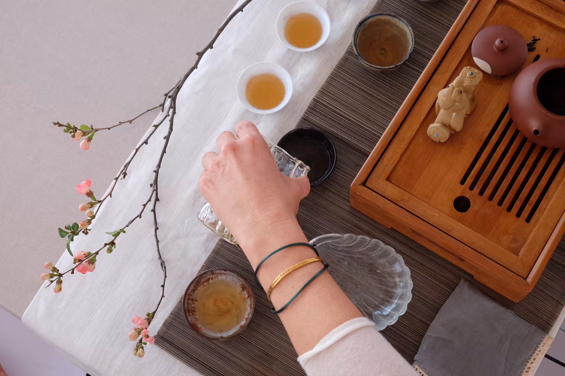 Top view of tea ceremony setup with wooden gongfu tray, clay teapot, tasting cups and floral branch decor