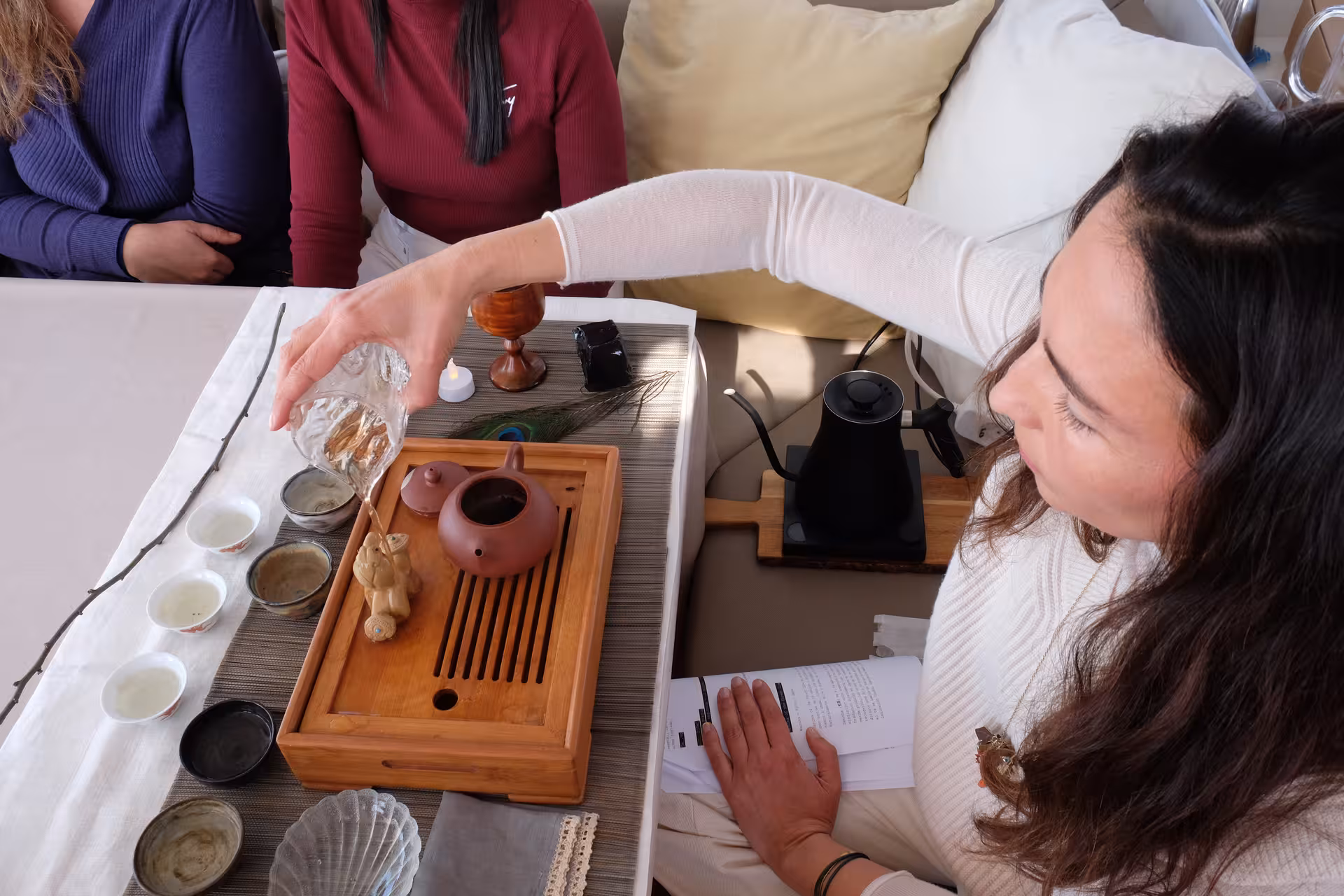Tea master pours hot water over loose leaf tea on a wooden tray during a hands-on tea ceremony workshop