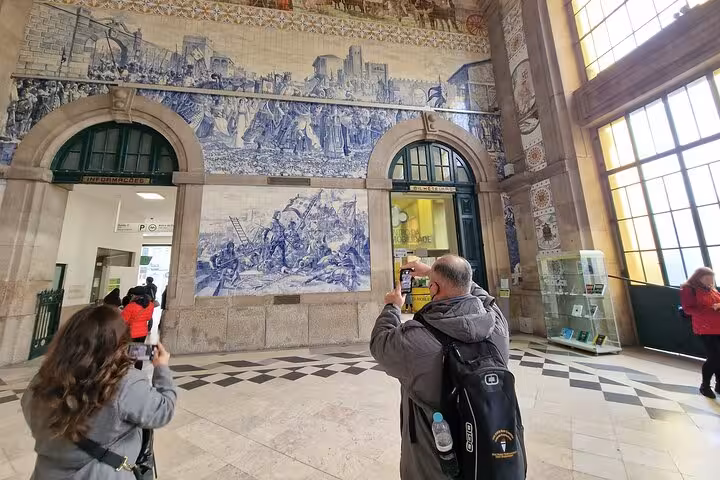 Travelers photographing Porto São Bento azulejo tiles, part of Three Shrines pilgrimage Fátima Santiago Nazaré