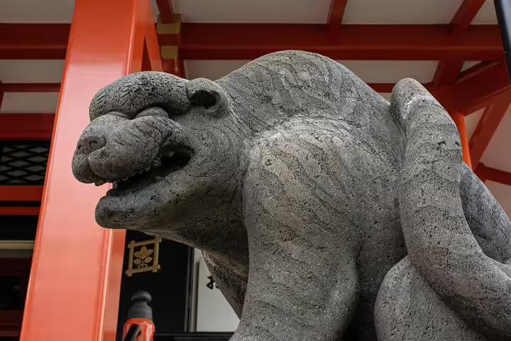 Stone guardian lion-dog statue at a Tokyo shrine with red torii gate structure behind