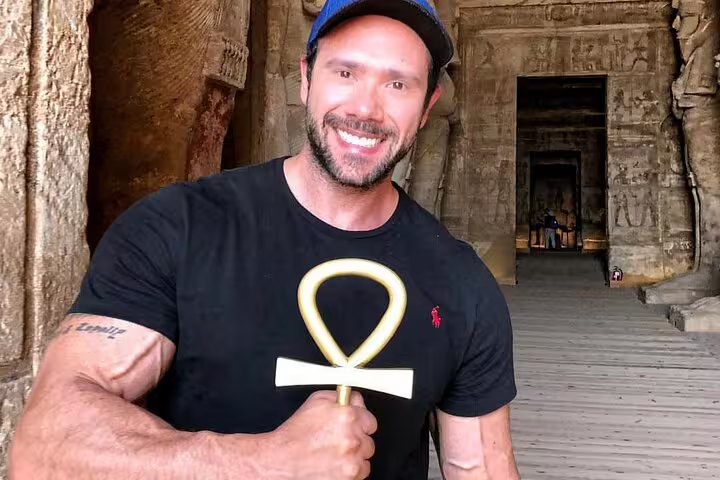 Smiling tourist holding ankh inside Abu Simbel temple corridor on guided day tour from Aswan, Egypt