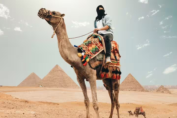 Tourist riding decorated camel with Giza Pyramids behind, classic Egypt day tour camel safari at the pyramids
