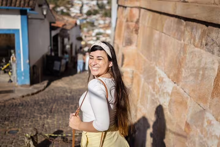 Smiling tourist walking along a charming cobblestone street in a historic town on Minas Gerais' Gold Route.