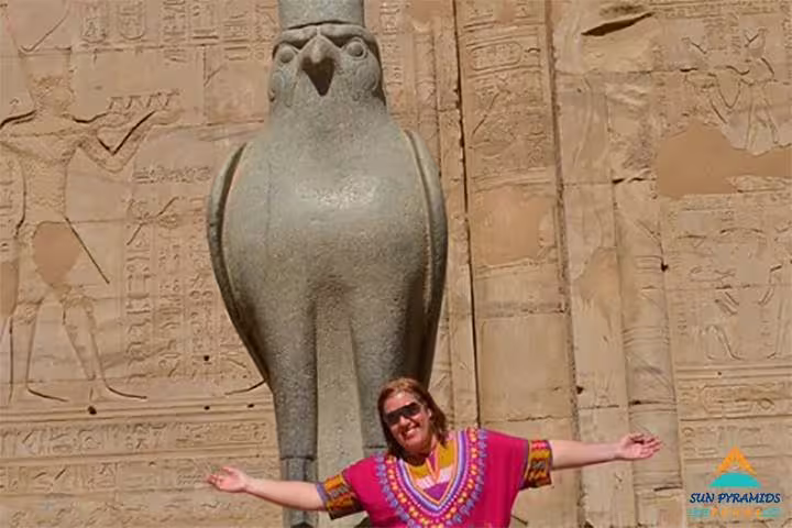 Tourist with arms open by Horus falcon statue and hieroglyphs at Edfu Temple on 8-day Nile cruise to Luxor