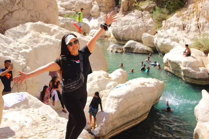 Happy tourist posing by a vibrant swimming spot in Oman's rocky landscape, highlighting a 3-day private tour experience.