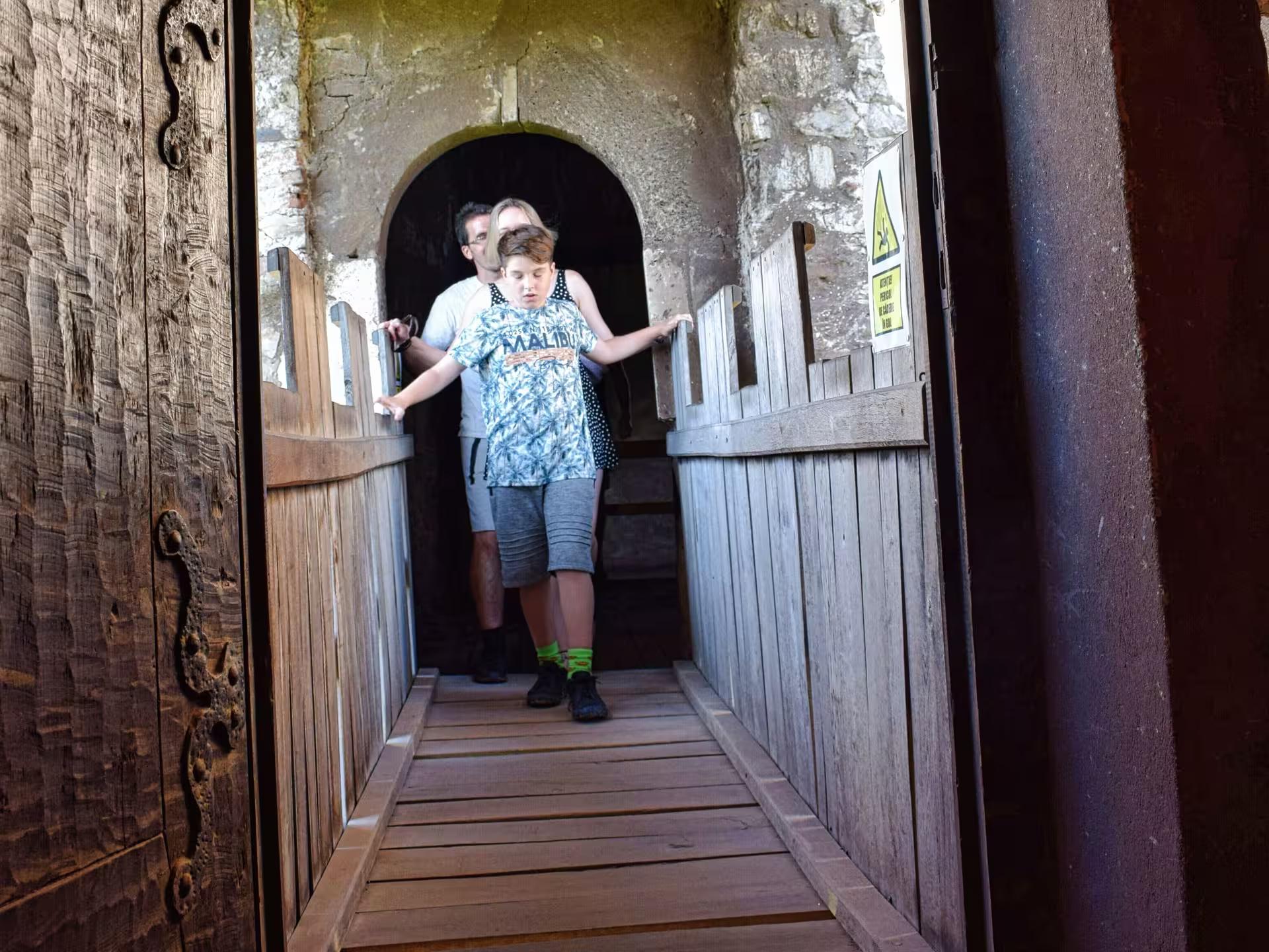 Tourists crossing a narrow wooden drawbridge passage inside a historic Transylvania castle on a guided castles tour