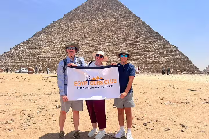 Tourists holding Egypt Tours Club banner in front of the Great Pyramid on a Giza half-day pyramids tour