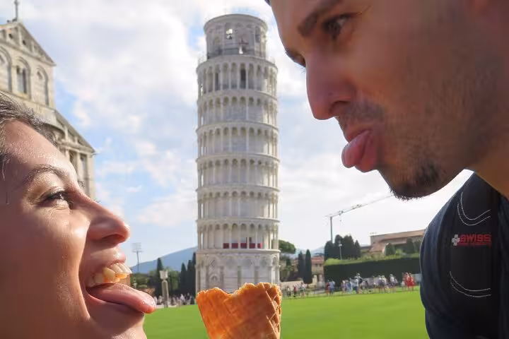 Playful tourists enjoy ice cream with the Leaning Tower of Pisa in the background on a sunny Tuscany tour.