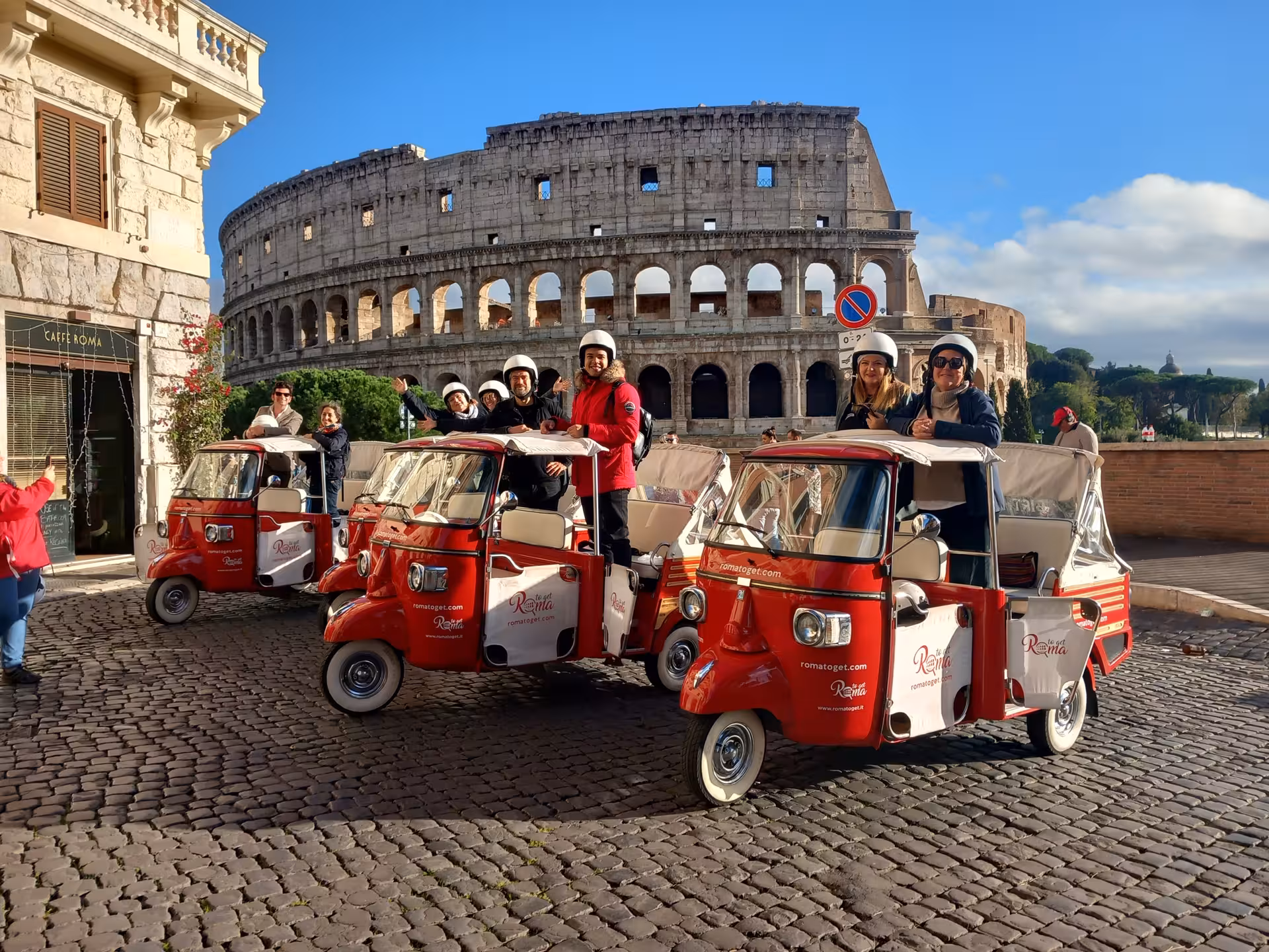 Group of tourists on red tuk-tuks in front of the Colosseum, highlighting a fun and scenic Rome sightseeing tour.