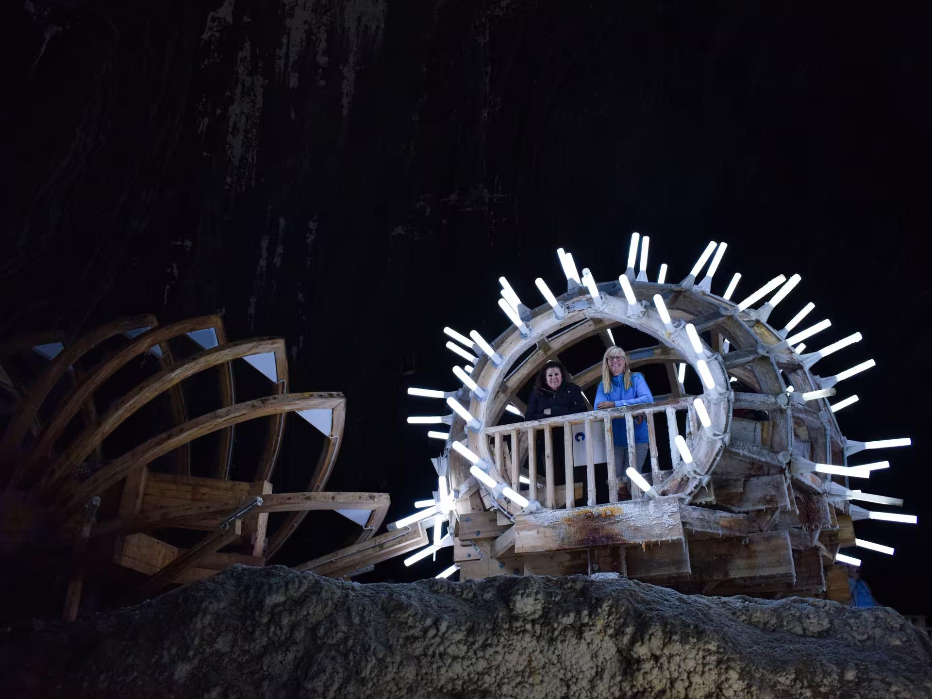 Tourists posing inside illuminated wooden wheel structure at Transylvania salt mine on a guided tour