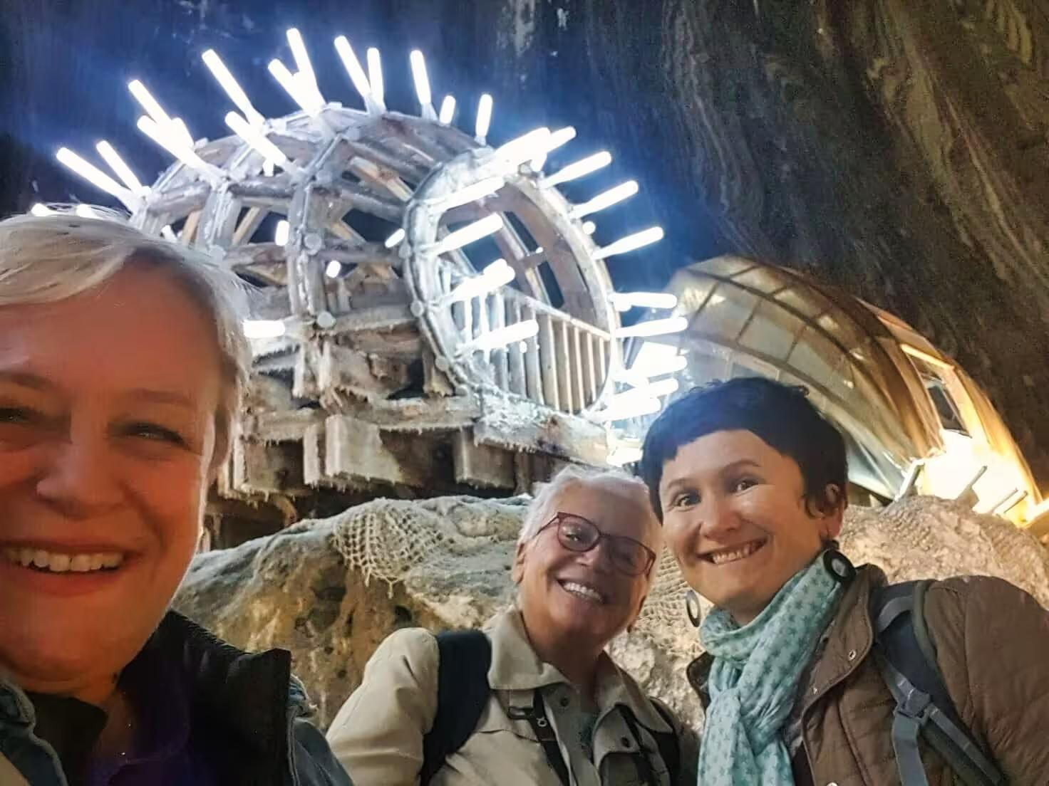 Happy tourists posing inside Turda Salt Mine near a lit wooden wheel on a guided tour from Cluj