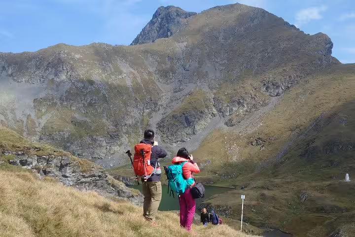 Two hikers with backpacks photographing a mountain lake on the Transfagarasan Road trail in Romania