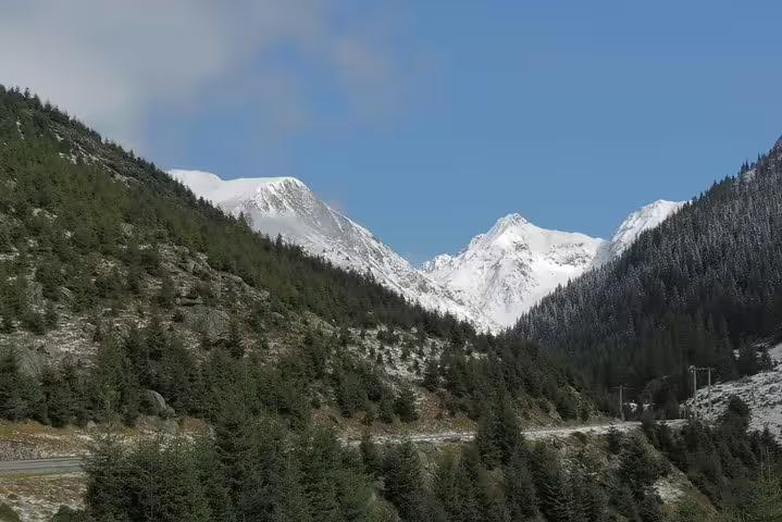 Snow-capped Fagaras Mountains with pine forests and winding road through Transfagarasan valley
