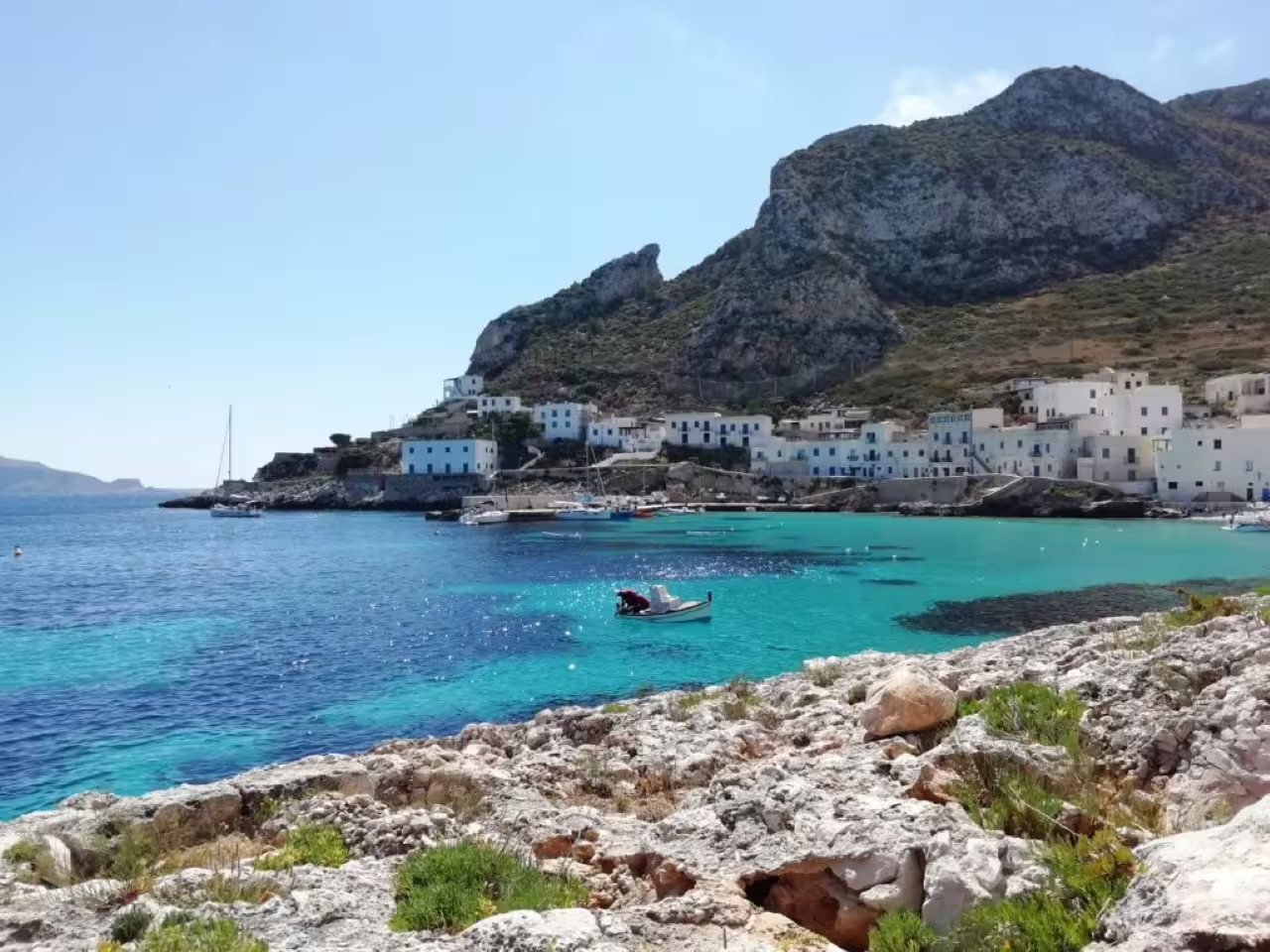 Crystal-clear bay on Favignana with white seaside village and cliffs, stop on Trapani mini-cruise to Levanzo