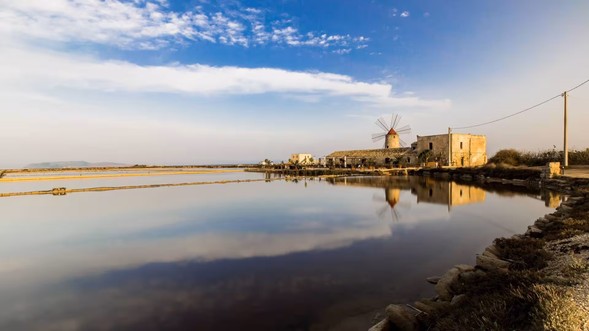 Historic windmill and salt flats reflecting in tranquil waters during an ebike tour from Trapani to Marsala.