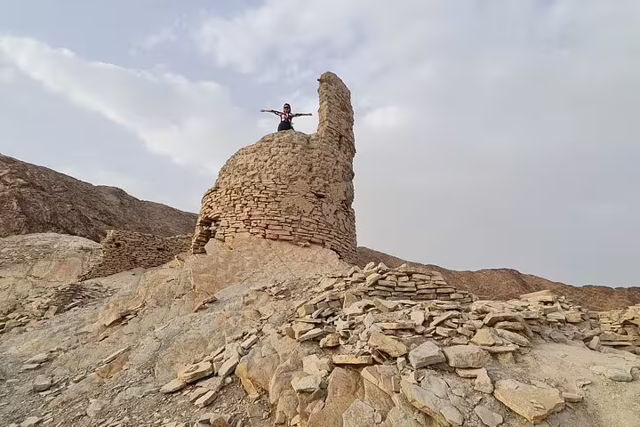 Traveler atop ancient stone tower amidst rocky landscape during a 3-day private Oman tour adventure.