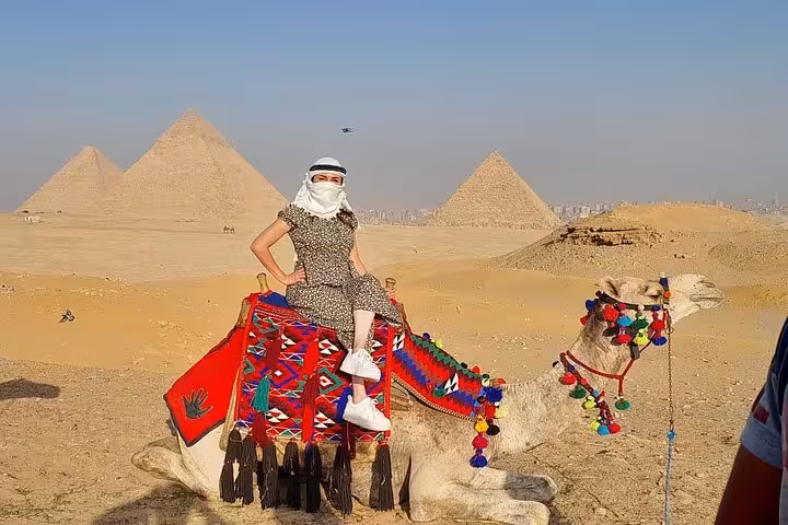 Traveler on decorated camel with Giza Pyramids backdrop, part of Cairo tour with ATV ride and felucca sailing
