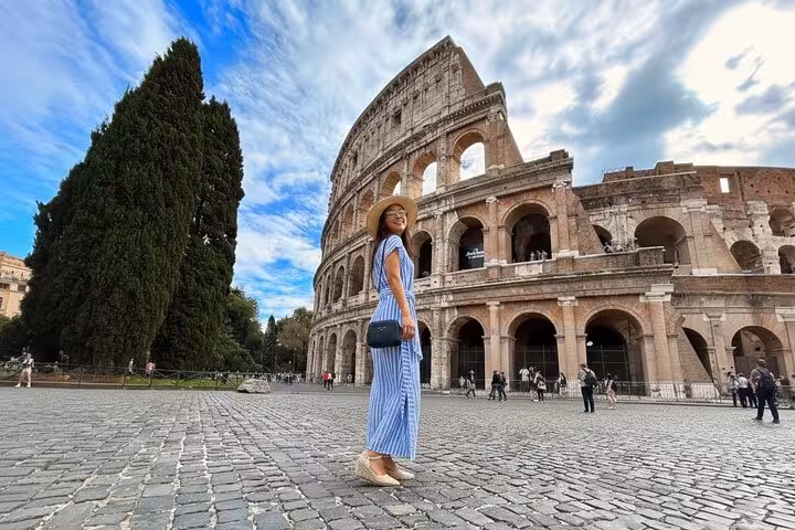 Traveler posing in front of the iconic Colosseum under a blue sky, a must-see on the Rome Highlights Tour.