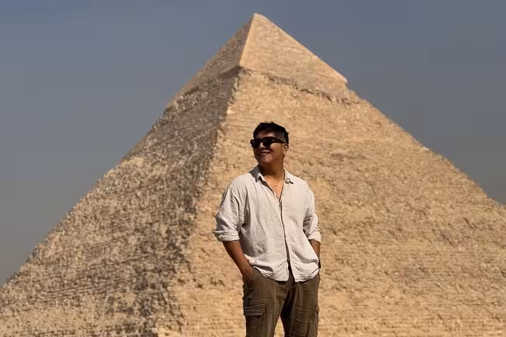 Traveler posing by the Great Pyramid of Khufu on half-day Giza Pyramids tour with 9-pyramids view stop
