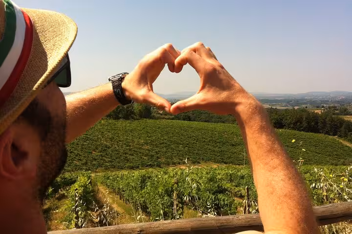 Traveler forms a heart with hands overlooking a lush Tuscan vineyard, capturing the essence of a scenic day trip.