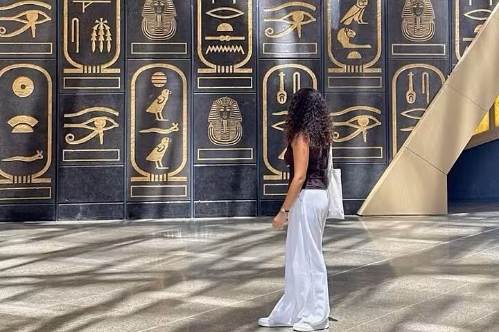 Traveler admiring ancient-style hieroglyph wall inside Grand Egyptian Museum on Hurghada to Pyramids tour