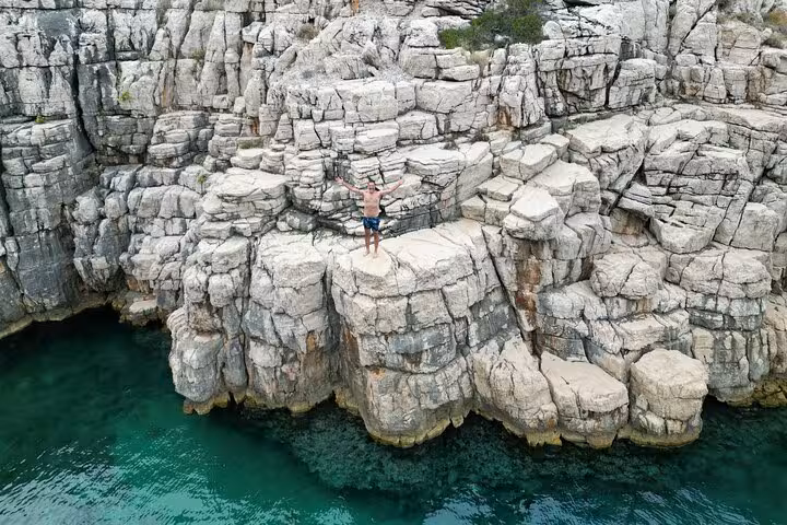 Traveler standing on rugged limestone cliffs above emerald Adriatic water, scenic stop on private boat tour Croatia