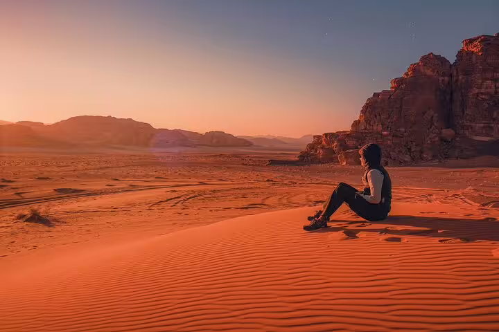 Traveler resting on red desert dunes at sunset, scenic stop on Petra tour from Taba by ferry boat