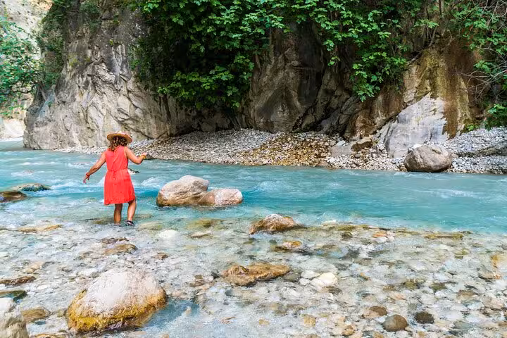 Traveler wades through turquoise waters of Saklıkent Canyon, surrounded by lush greenery and rugged cliffs.