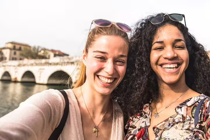 Two travelers smiling by Pisa river on a self-guided e-scavenger hunt, exploring the city at your own pace