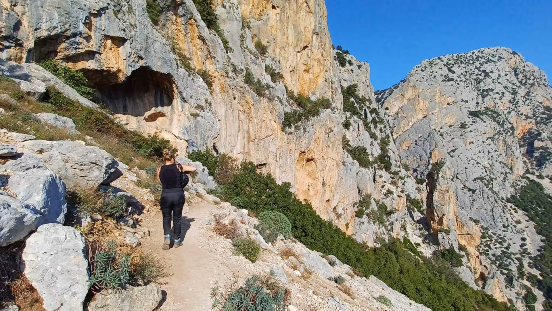 Trekker walking along scenic Gorropu Canyon trail with dramatic cliffs and natural beauty.