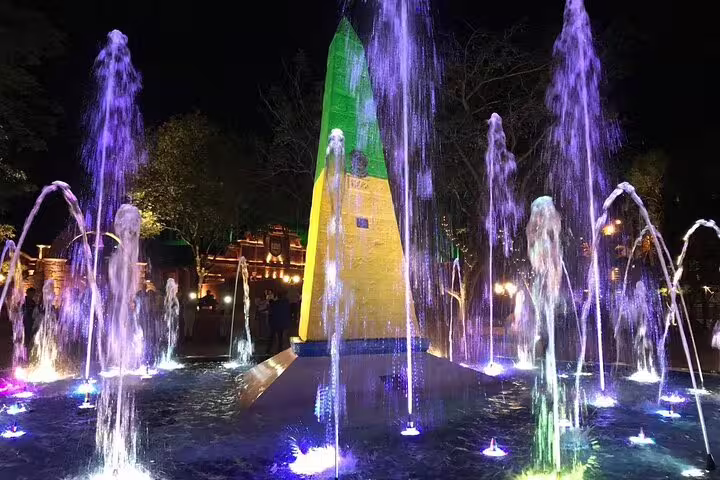 Illuminated fountains and colorful obelisk light up Tres Fronteiras landmark at night, showcasing vibrant water displays.