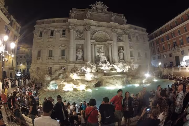 Tourists admire the illuminated Trevi Fountain at night, a highlight of the exclusive private Vespa tour in Rome.