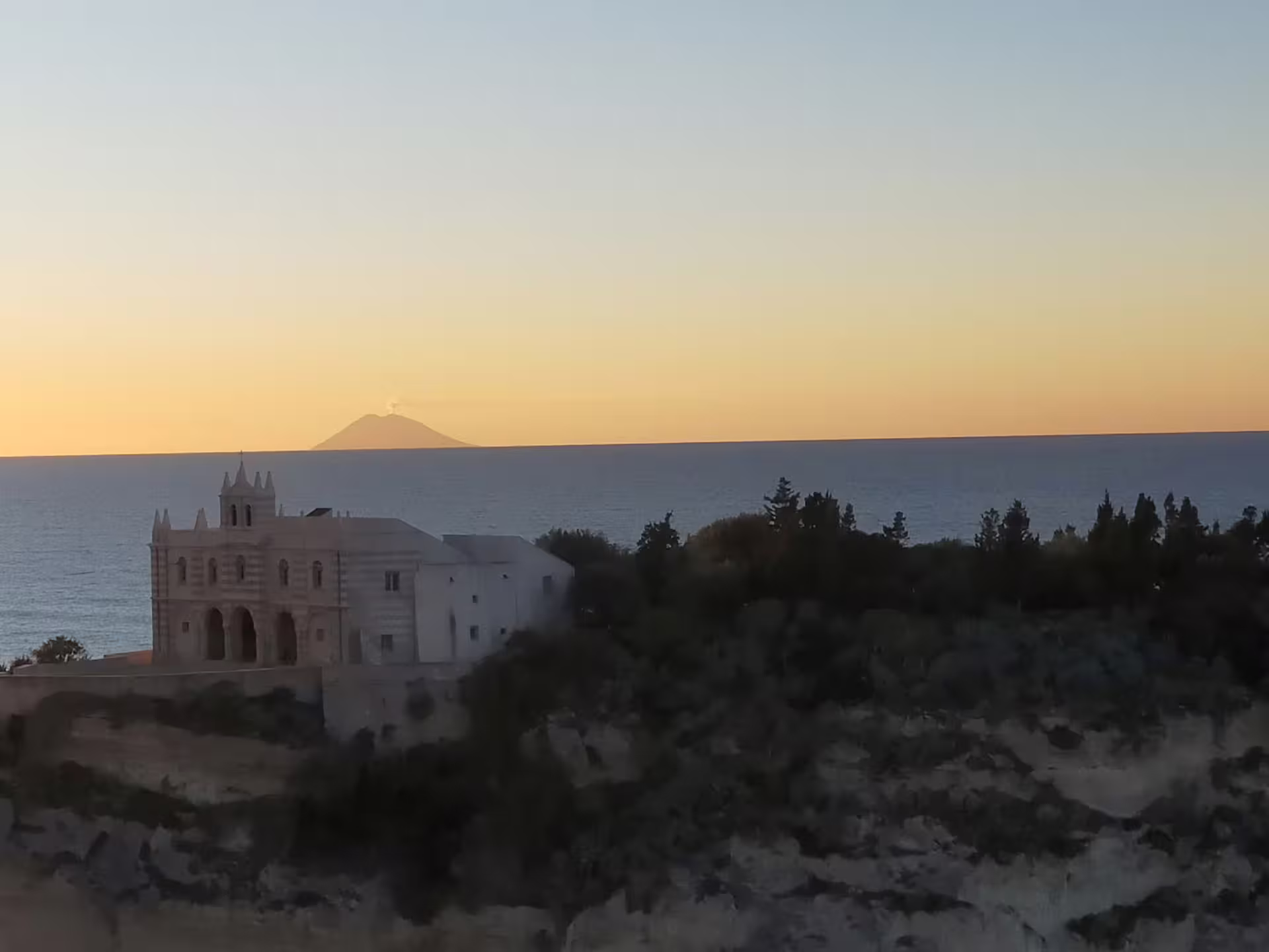 Sunset over Tropea coastline with clifftop sanctuary and Stromboli volcano on the horizon, featured on Divine Calabria tour
