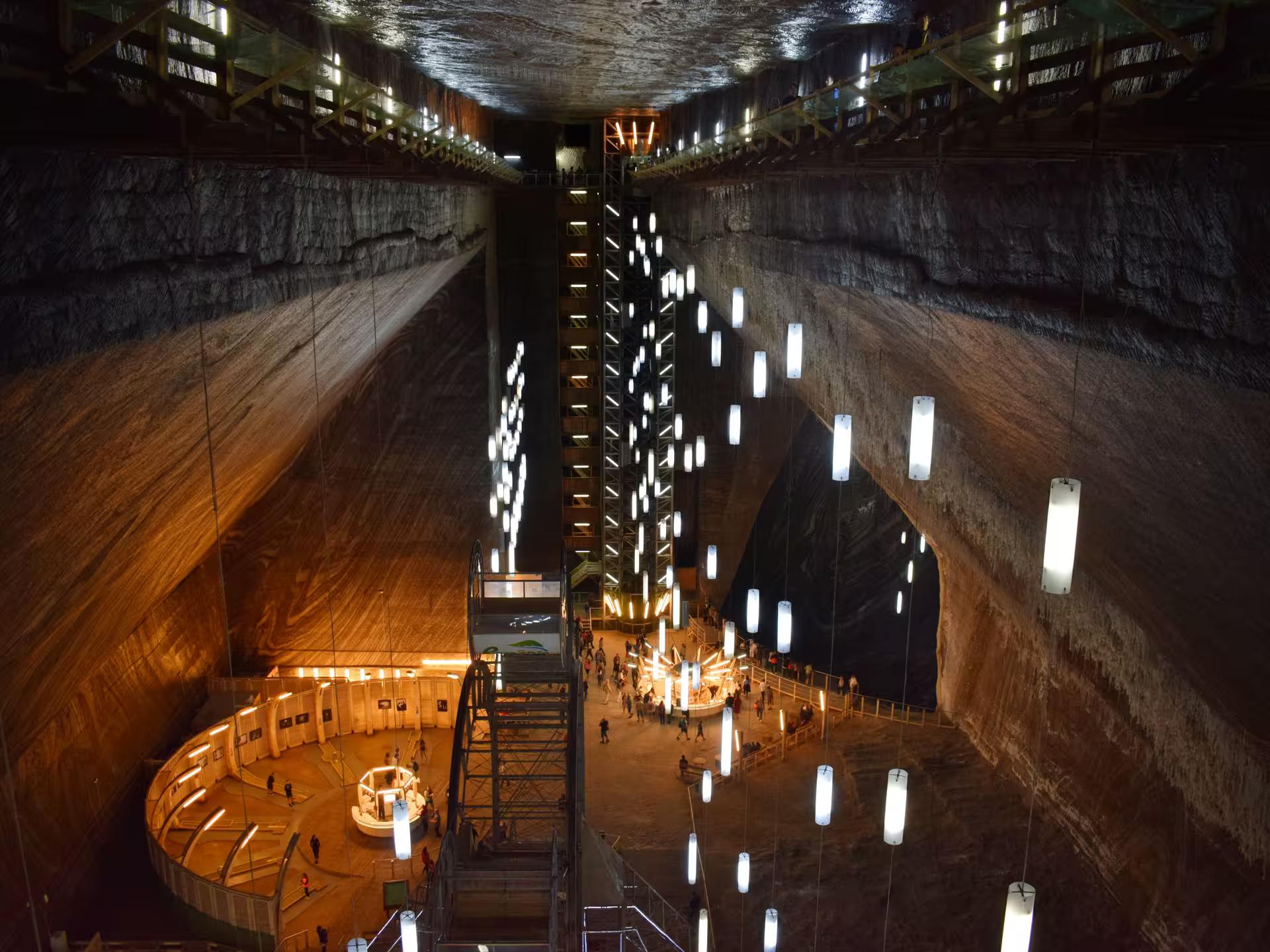 Stunning illuminated vast underground chamber of Turda Salt Mine with hanging lights and visitors exploring from Cluj guided tour