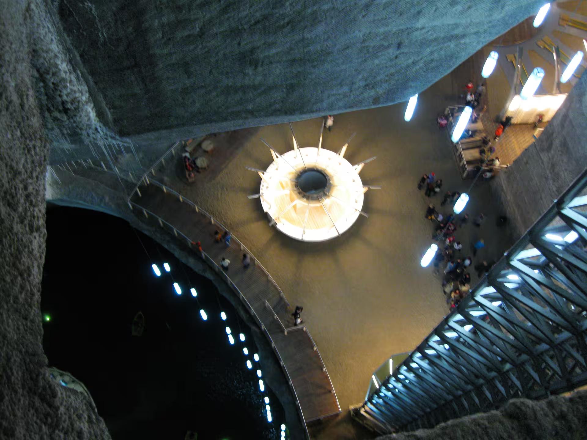 Aerial view of Turda Salt Mine underground chamber with glowing central light and visitors exploring ancient salt caverns in Romania