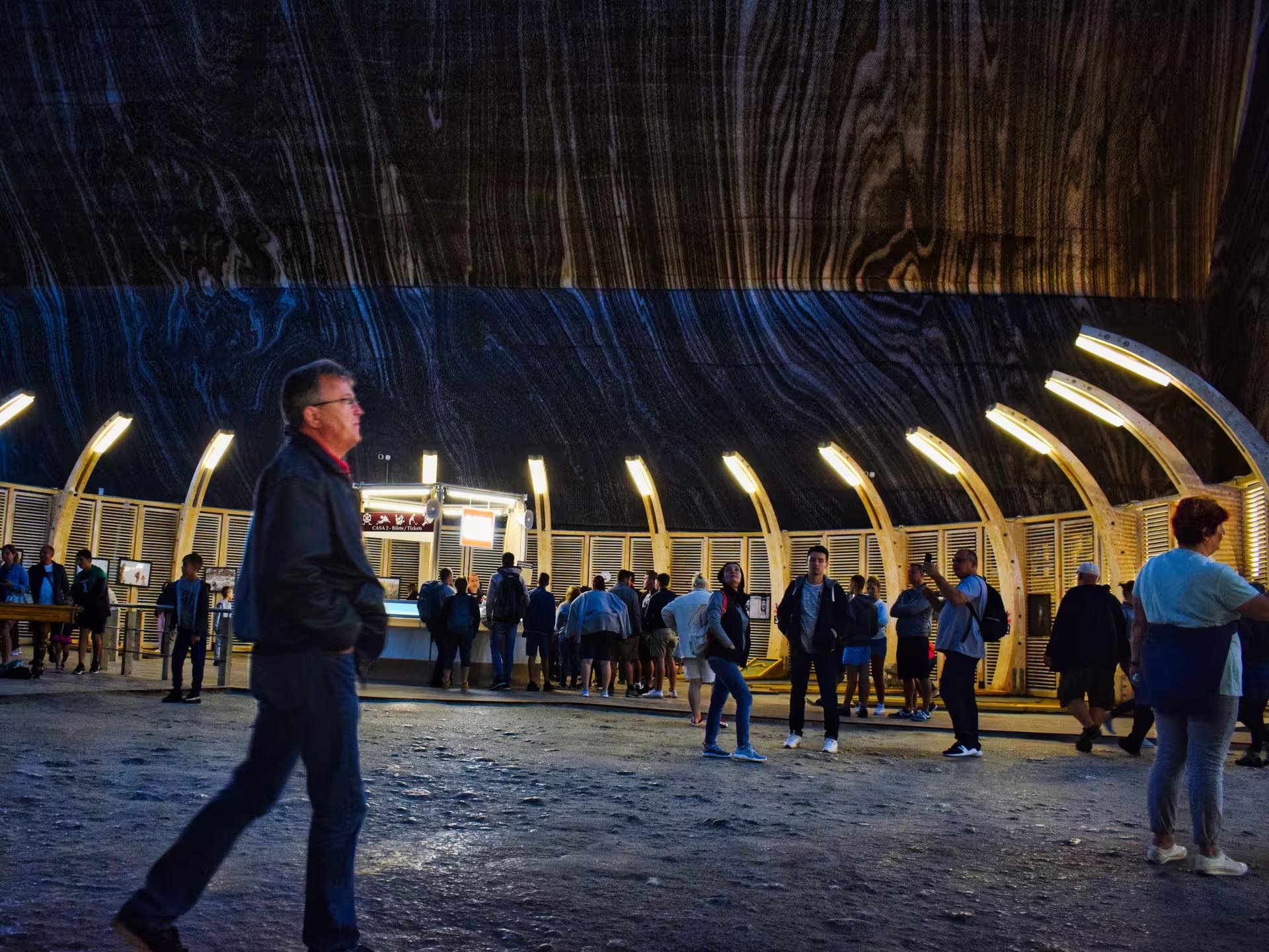 Tourists exploring the illuminated underground entrance hall of Turda Salt Mine on a guided tour from Cluj