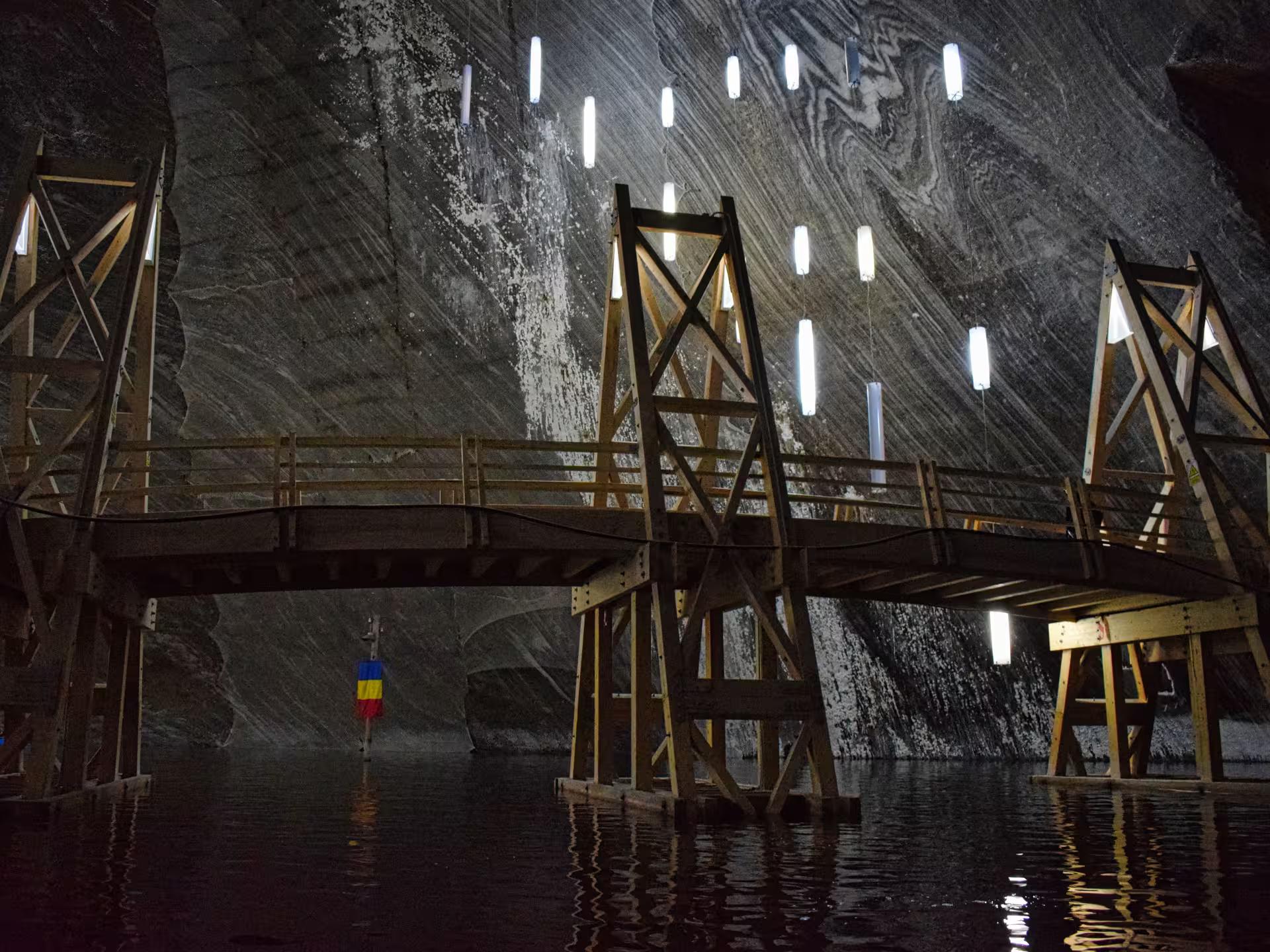 Wooden bridge over underground lake inside Turda Salt Mine with swirling salt walls on a Romania full-day tour