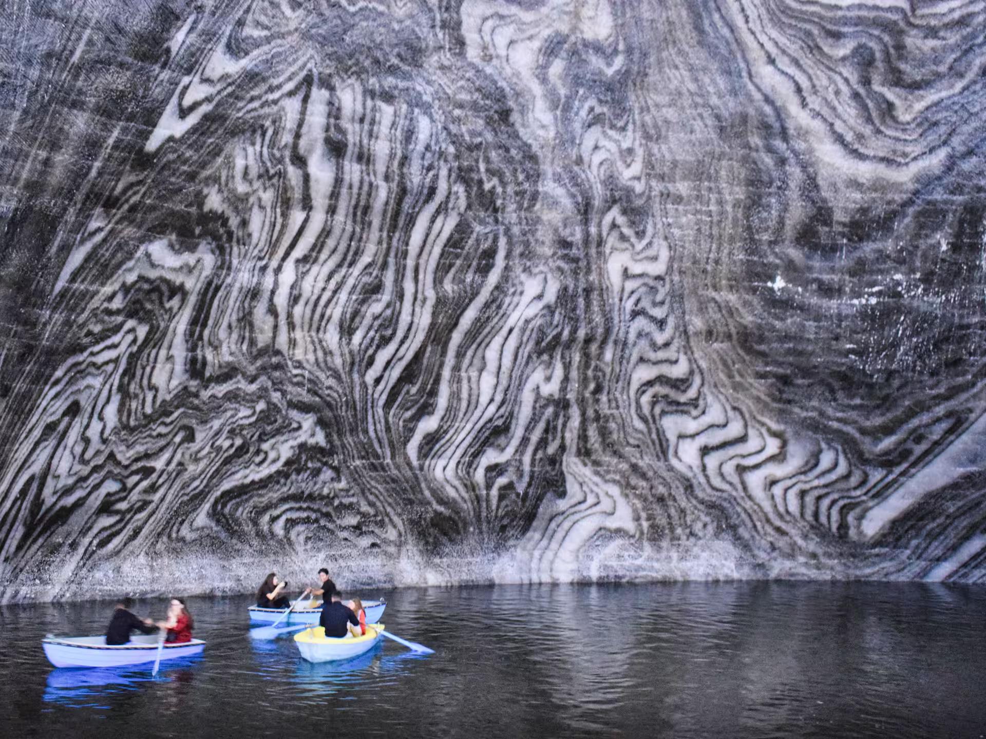 Visitors rowing boats on the underground lake at Turda Salt Mine with stunning swirling salt rock walls on a full-day Romania tour