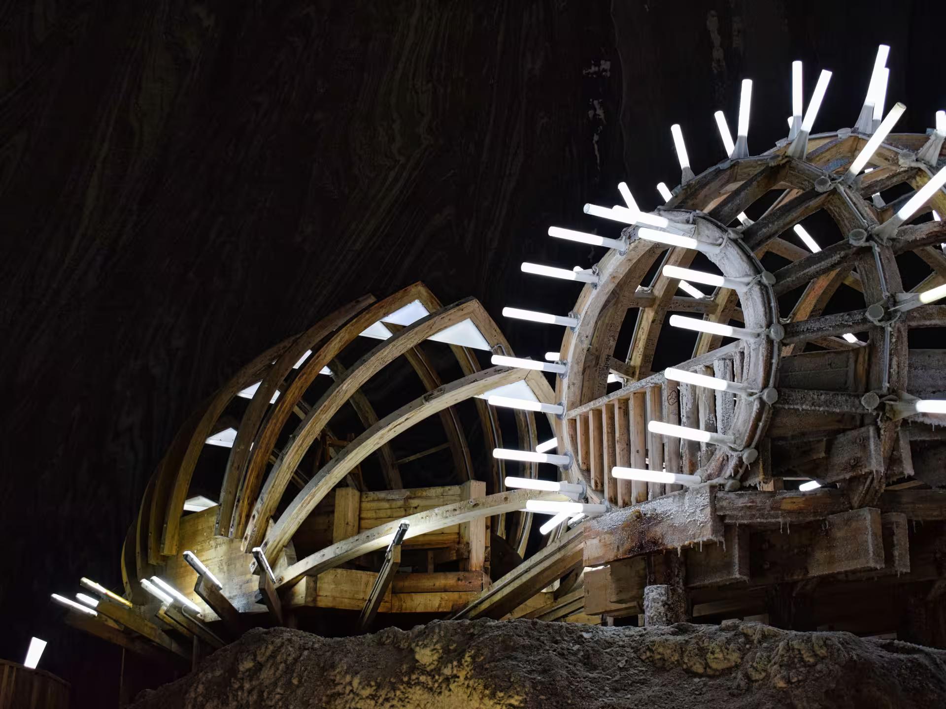 Historic wooden wheel structure illuminated by LED lights deep inside Turda Salt Mine Romania full-day tour