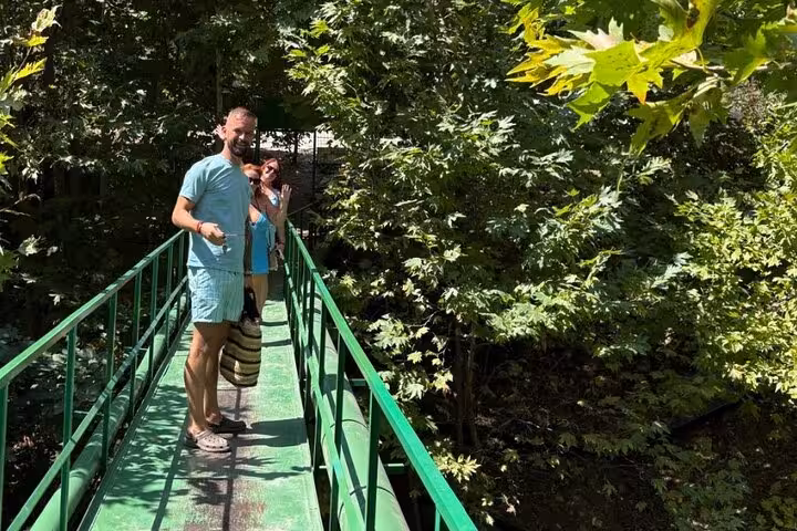 Visitors enjoy a peaceful walk on a lush green bridge surrounded by vibrant foliage in a Turkish village.