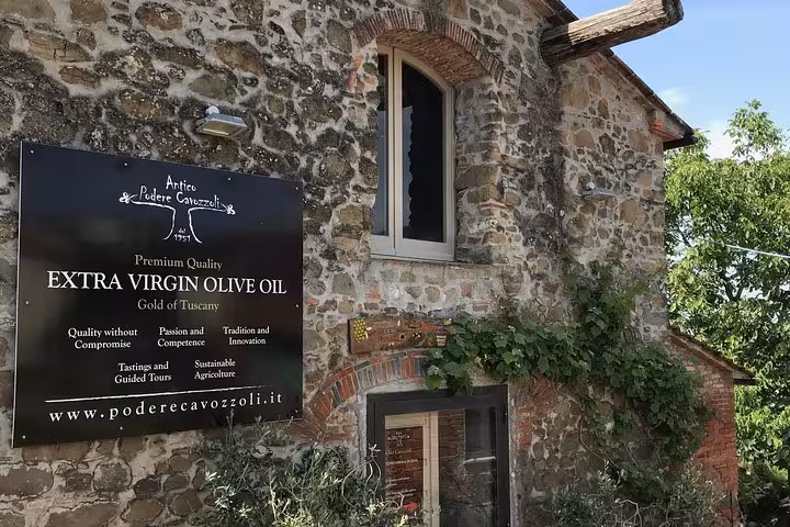 Historic Tuscan stone building with a sign promoting premium extra virgin olive oil and guided tours.