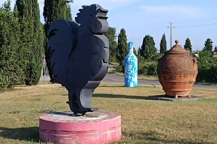 Outdoor winery sculptures of a rooster, wine bottle and clay urn on a grassy estate, welcoming guests to vineyard tours